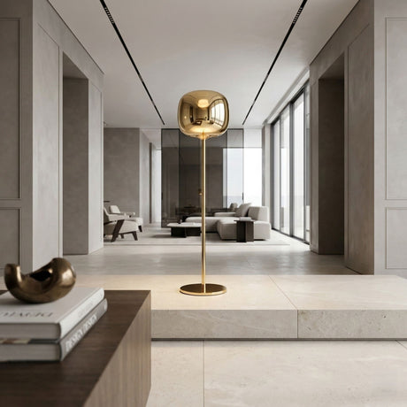A modern living room with minimalist decor features the Dusk Dawn LED Floor Lamp - Gold as a centerpiece, paired with neutral furniture, large windows, and sleek LED lighting above the coffee table adorned with books and a sculpture.