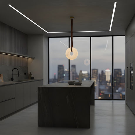A modern kitchen with dark cabinets, a marble island, minimalist decor, and the Cintura LED Large Alabaster Single Pendant Light (Soft White & Brown). Large windows showcase a city skyline at dusk with glowing buildings beyond.