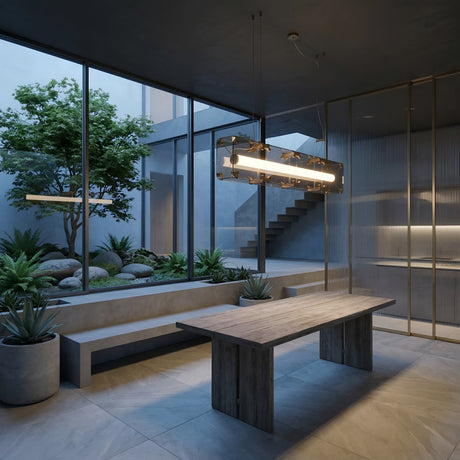 A modern indoor dining area features a wooden table, concrete benches, potted plants, and floor-to-ceiling windows overlooking a minimalist courtyard. The Qbic LED Large Linear Suspension Light - Clear hangs above the table for a sleek, contemporary touch.