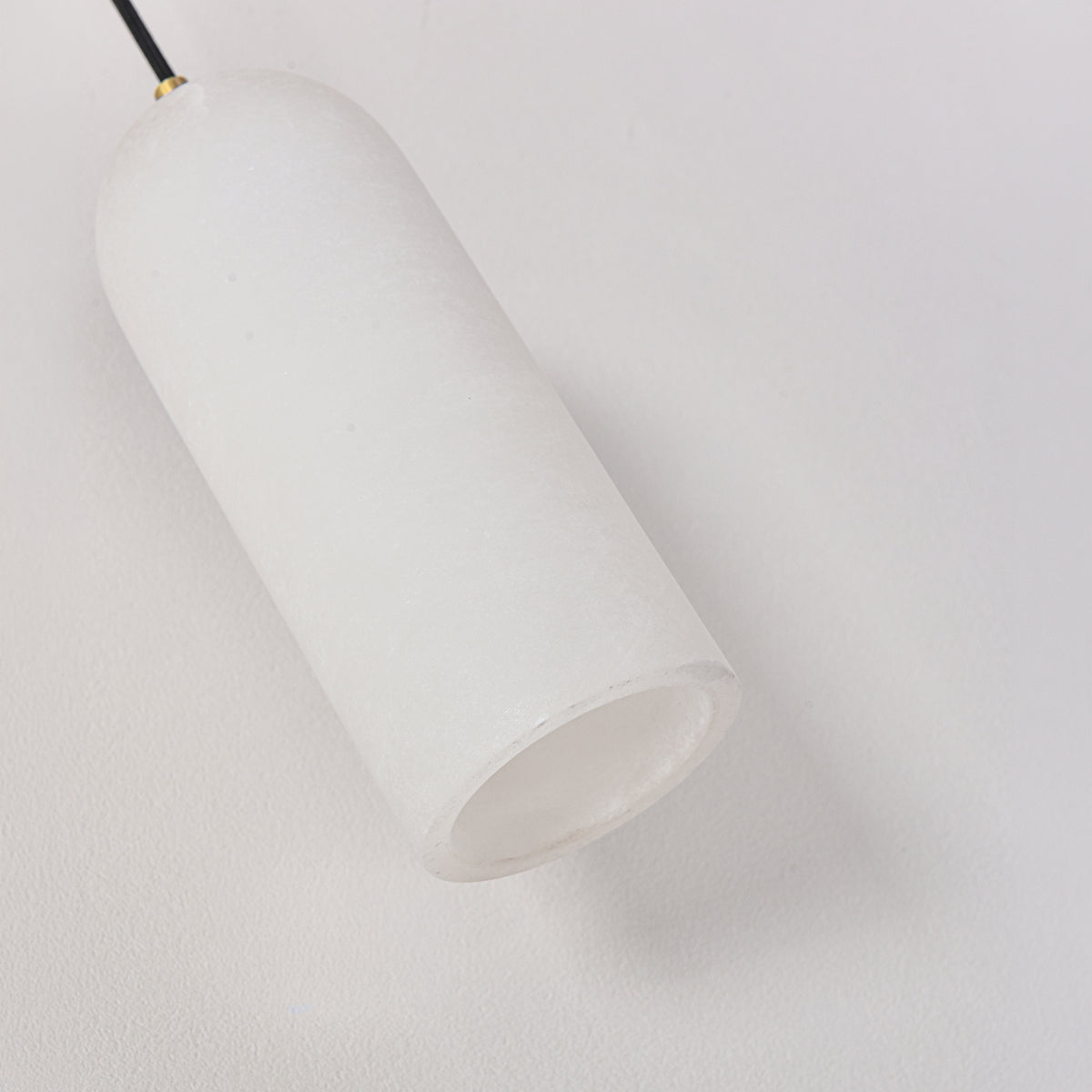 Velmora slim cylindrical alabaster pendant light in soft white, with brass ceiling plate and black flex, shown close-up against a plain background.