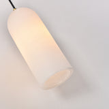 Velmora slim cylindrical alabaster pendant light with soft white stone shade, black flex, and brass ceiling fitting, glowing warmly against a plain light background.