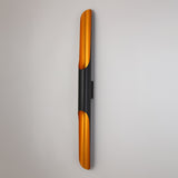 The Stealth 2 Light Wall Light - Brass & Black is a modern wall-mounted fixture featuring brass ends and a matte black center, creating a sleek, contemporary look when installed on a white wall.