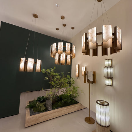 Caelith 10 Light Large Panel Alabaster Chandelier in brushed brass, shown suspended in a showroom alongside matching pendant lights and wall sconces with glowing alabaster panels.