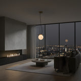A modern living room at night features minimalist furniture, a round coffee table, and floor-to-ceiling windows with city views, softly lit by the Marenzo 1 Light Small Orb Alabaster Single Pendant Light in Soft White & Brushed Brass beneath the full moon.