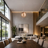A modern living and dining area with high ceilings, large windows, a dark wood table, beige chairs, and a cozy sectional is beautifully lit by the Elon LED Single Pendant - Copper and natural light for an elegant ambiance.
