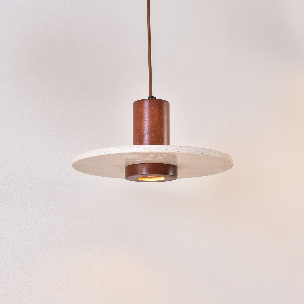 Torvane 1 Light Travertine Disc Pendant Light with a light beige stone disc and walnut brown wooden column, glowing centre light, on a plain white background.