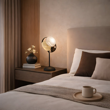 A modern bedroom with a neatly made bed, neutral bedding, a wooden nightstand featuring the Selvano 1 Light Globe Alabaster Table Lamp in soft white & matte black, a vase of flowers, stacked books, and a mug on a tray.