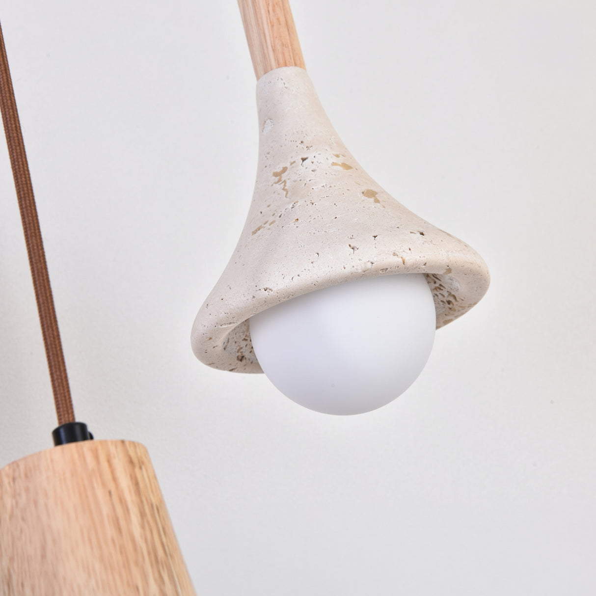 Vantoro pendant light close-up showing the travertine cone shade with natural pitted texture over a white globe bulb, wood stem, against a plain light background.