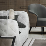 Paros Alabaster Table Lamp in white, with a slim iron stem and hanging alabaster shade, shown beside a tufted white sofa and grey armchair in a living room setting.