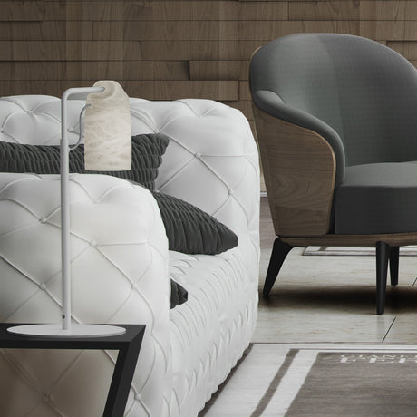 Paros Alabaster Table Lamp in white, with a slim iron stem and hanging alabaster shade, shown beside a tufted white sofa and grey armchair in a living room setting.