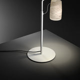 Paros Alabaster Table Lamp in white, with a round base, slim curved stem, and a hanging alabaster shade with soft grey veining, glowing against a dark background.