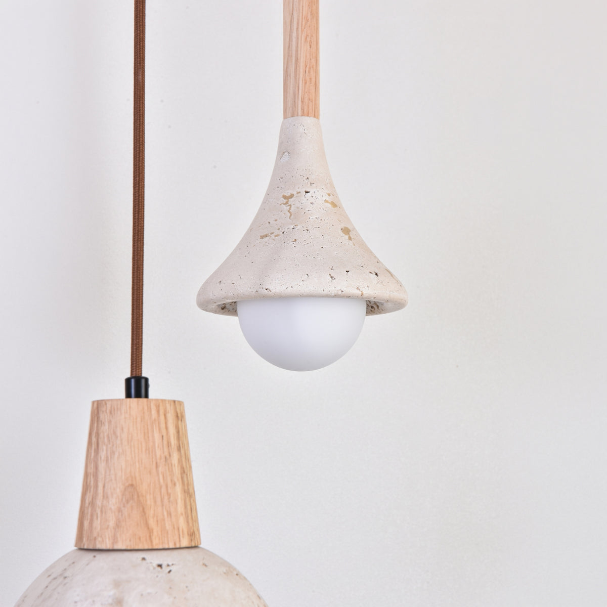Vantoro pendant light with a cone-shaped travertine shade in light beige, wood stem, and exposed opal globe bulb, shown beside a second pendant with a rounded wood cap and stone-look shade.