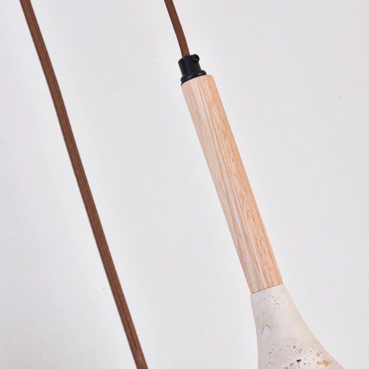 Close-up of the Vantoro pendant light's wood stem in light beige with black cap fitting, brown braided cable, and travertine cone shade edge visible below, set against a plain white background.