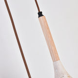 Close-up of the Vantoro pendant light's wood stem in light beige with black cap fitting, brown braided cable, and travertine cone shade edge visible below, set against a plain white background.