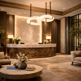 A luxurious hotel lobby with modern decor featuring a marble reception, elegant circular chandelier, Serava LED Small Alabaster Loop Suspension Lights in brown & soft white, plush seating, floral accents, and soft ambient lighting.