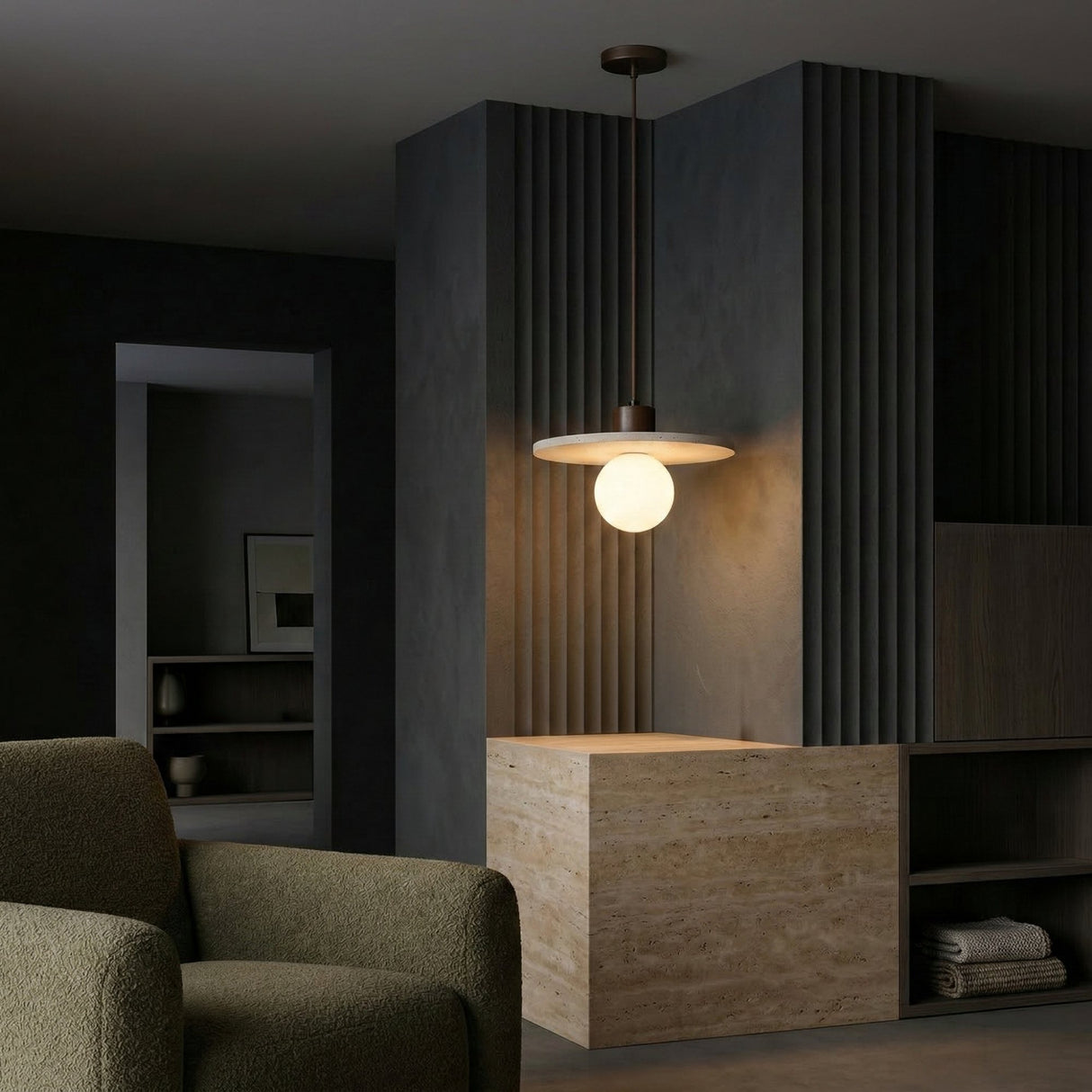 A modern, minimalistic interior featuring the Torelli 1 Light Wide Disc Travertine Pendant Light in Walnut Brown & Light Beige above a marble-topped counter, dark paneled walls, and an olive-green armchair in the foreground.