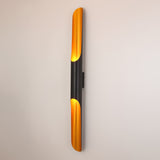 The Stealth 2 Light Wall Light in Brass & Black features a sleek vertical design with brass accents, casting warm light against a plain white wall.