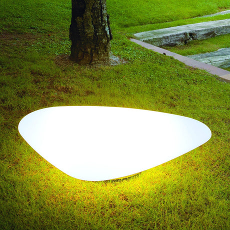 Stone LED outdoor floor lamp in white, smooth pebble-shaped design glowing on grass beside a tree trunk, integrated LED, IP45 rated.