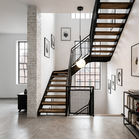 Modern interior with a black metal and wood staircase, white brick accent wall, large windows, abstract framed art, the Vetra Opal Glass Small Pendant Light - Black, minimalistic decor, and light gray concrete floors.
