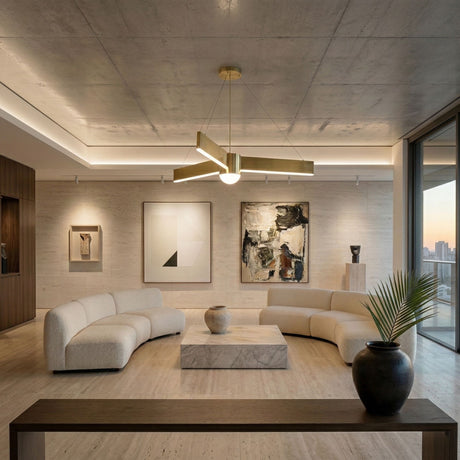 A modern living room with curved white sofas, a marble coffee table, abstract wall art, and a large potted plant features floor-to-ceiling windows with a city skyline at sunset. The Fritz LED Suspension Light - Matte Gold hangs from the concrete ceiling.