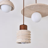 Rivano Ribbed Travertine Pendant Light with a ridged light beige stone drum, walnut wood top, and opal globe bulb, shown alongside matching disc-style pendants.