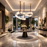 Luxurious modern foyer featuring a round table, floral arrangement, marble floors, spiral staircase, floor-to-ceiling windows with greenery views, and the Serava LED Large Alabaster Asymmetric Suspension Light in Brown & Soft White for elegant ambiance.