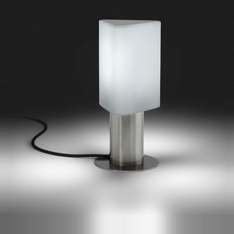 Tiny Triangle Table Lamp in satin nickel with a frosted triangular plastic shade, lit from within, on a cylindrical metal base with round foot, shown against a dark background.