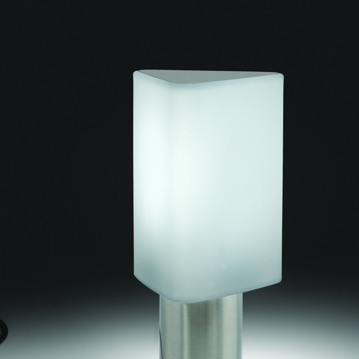 Tiny Triangle Table Lamp in Satin Nickel, with a glowing white plastic triangular shade and rounded corners on a slim cylindrical metal base, shown against a dark background.