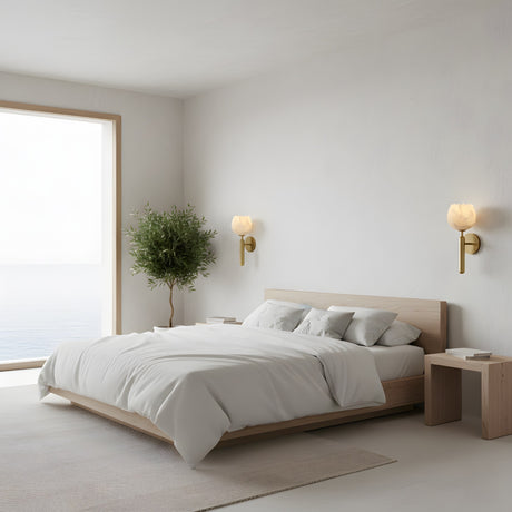 Minimalist bedroom with a wooden bed and white bedding, two wooden nightstands, a potted tree by a large ocean-view window, and Olivaro 1 Light Pedal Form Alabaster Wall Lights in Soft White & Brushed Brass above the bed.