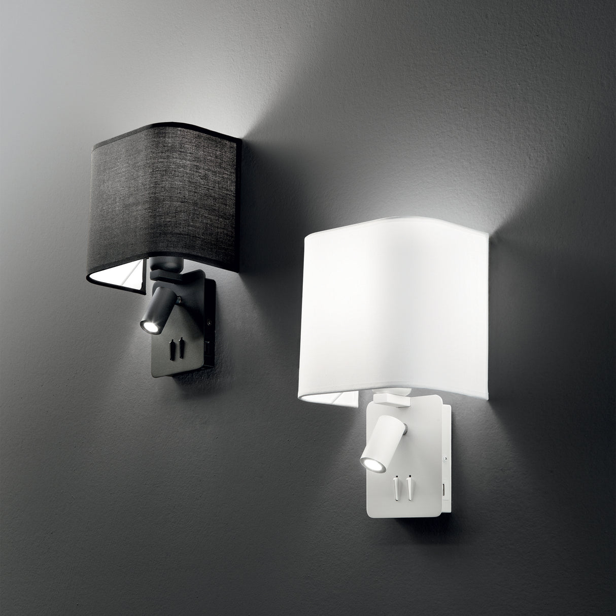 Displayed are two contemporary Prismia LED Wall Lights, perfect for chic modern interiors. One has a black rectangular shade and the other a white one, both elegantly mounted on a gray wall and featuring an adjustable 3W 3000K LED reading light at the base.