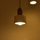Torvella Travertine Drum Wall Light with light beige travertine drum shade suspended from a walnut brown backplate, illuminated with a warm glow against a plain wall.