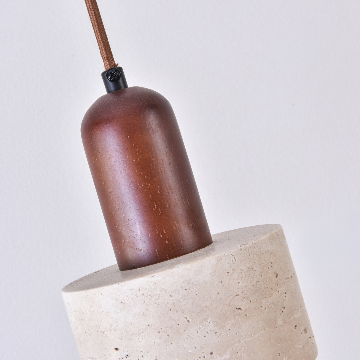 Close-up of the Torvella wall light's walnut brown drum socket cap suspended by a fabric flex above its light beige travertine base, shown against a plain white background.