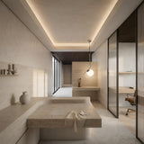 A modern minimalist bathroom with beige stone surfaces, a built-in sink, and a towel. The Vetra Opal Glass Large Pendant Light - Grey provides soft indirect light as a frosted glass wall separates it from the bright office area with desk and chair.
