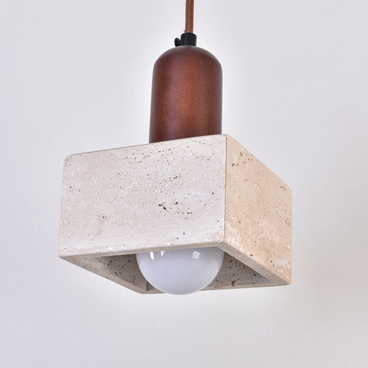 Cavero pendant light with square light beige travertine block base, rounded walnut brown wood top, and exposed globe bulb, shown on a plain white background.