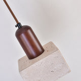 Cavero pendant light with a square light beige travertine block and rounded walnut brown wood top, suspended from a braided cord against a plain background.