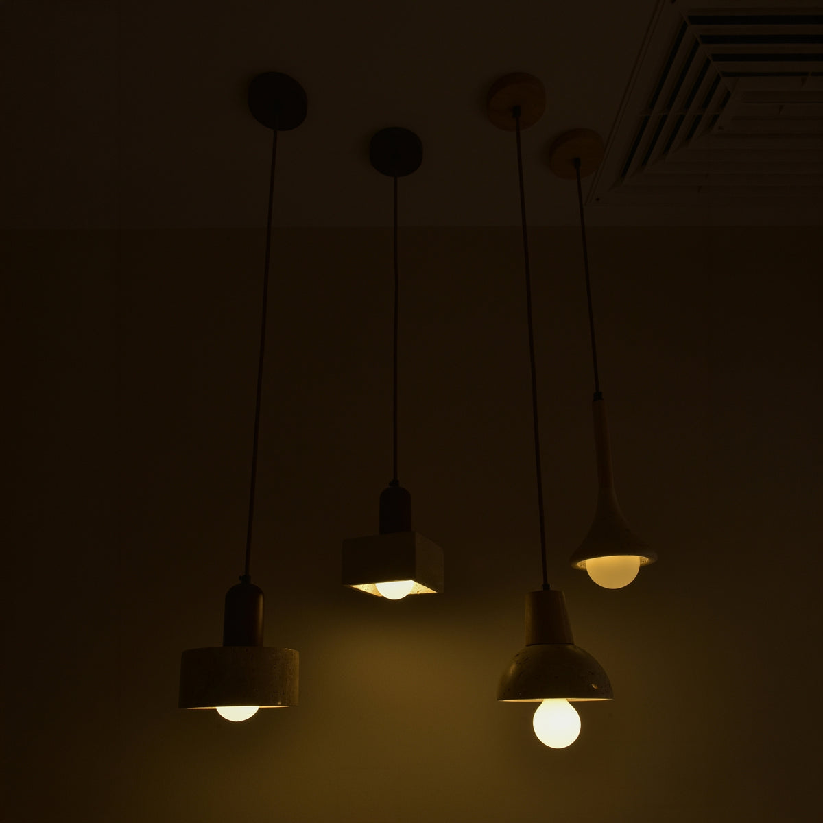 Lunaro Travertine & Walnut Single Pendant Light with cylindrical beige travertine shade and walnut cap, shown lit alongside other pendants on brown cords in a dim room.