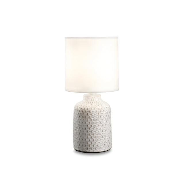 The Glimmerlux Large Table Lamp - White features a textured ceramic base paired with a cylindrical white fabric lampshade, providing a gentle, warm illumination. Its geometric pattern adds to the lamp's decorative charm, making it both practical and fashionable in any contemporary environment.