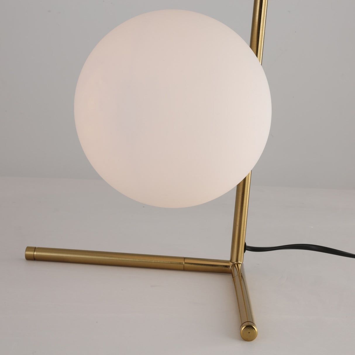 The Vetra 1 Light Opal Glass Table Lamp features a round opal diffuser and a gold-finished base, resting on a white surface with a visible black power cord.