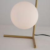 The Vetra 1 Light Opal Glass Table Lamp features a round opal diffuser and a gold-finished base, resting on a white surface with a visible black power cord.