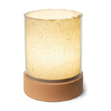 PotLight Glass Table Lamp in terracotta with round ceramic base and layered clear-and-frosted glass cylinder shade, glowing softly against a plain white background.