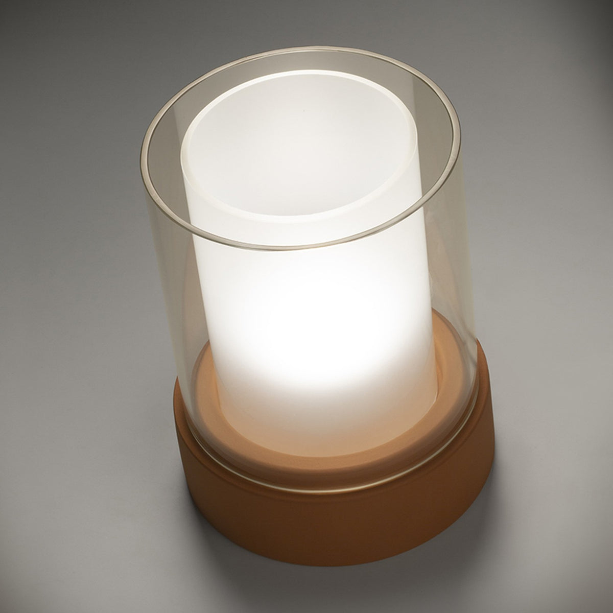 PotLight Glass Table Lamp in terracotta, round ceramic base with clear outer glass cylinder and frosted inner cylinder glowing softly, shown on a plain grey background.