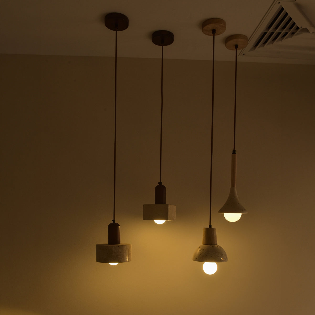 Lunaro 1 Light Travertine Pendant Light in walnut and light beige, shown among similar pendants with a cylindrical stone shade lit warmly against a neutral wall.