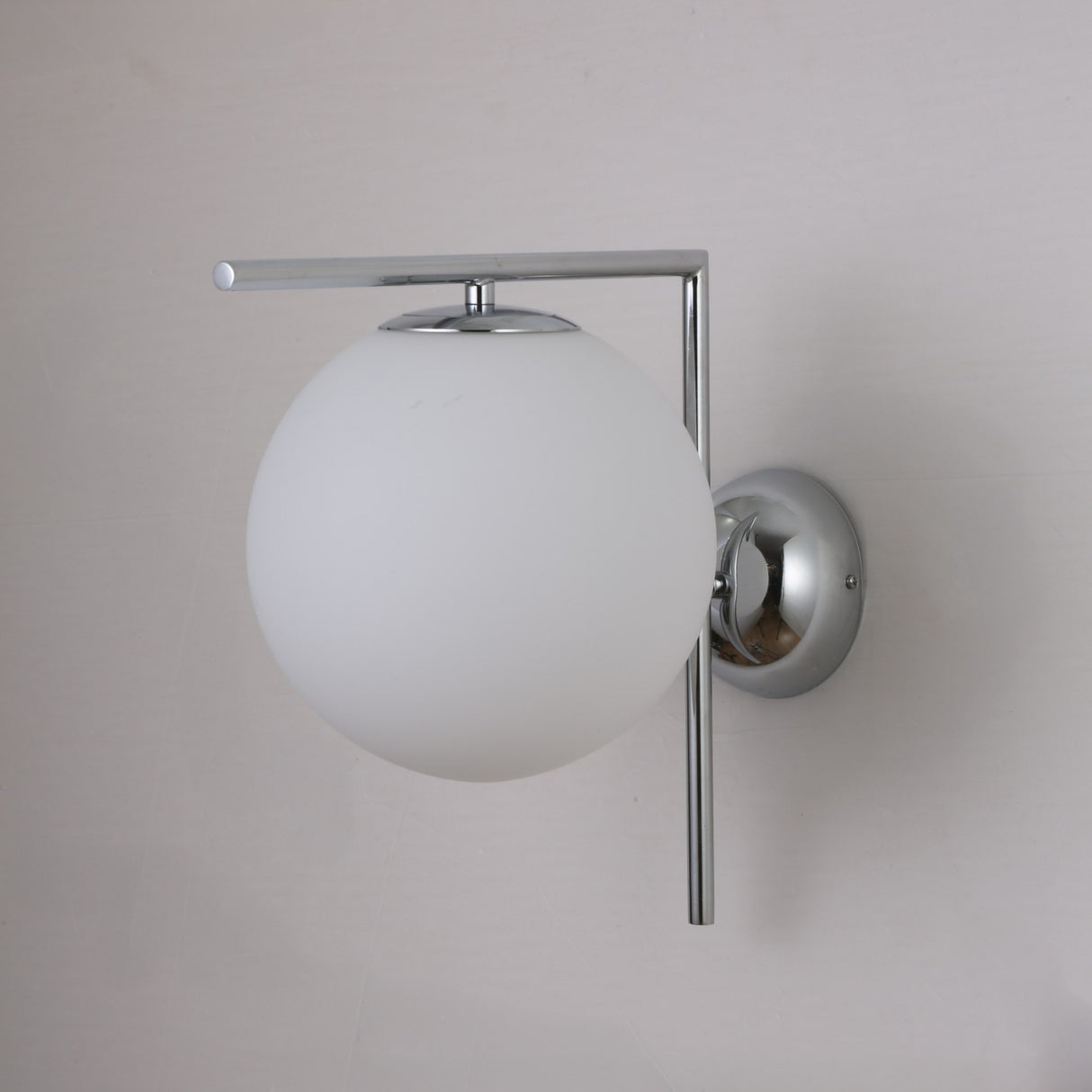 The Vetra 1 Light Opal Glass Wall/Semi-Flush Ceiling Light in Grey features a modern, Nordic-inspired design with a frosted glass globe and sleek metallic details, mounted on a round chrome base against a light wall.