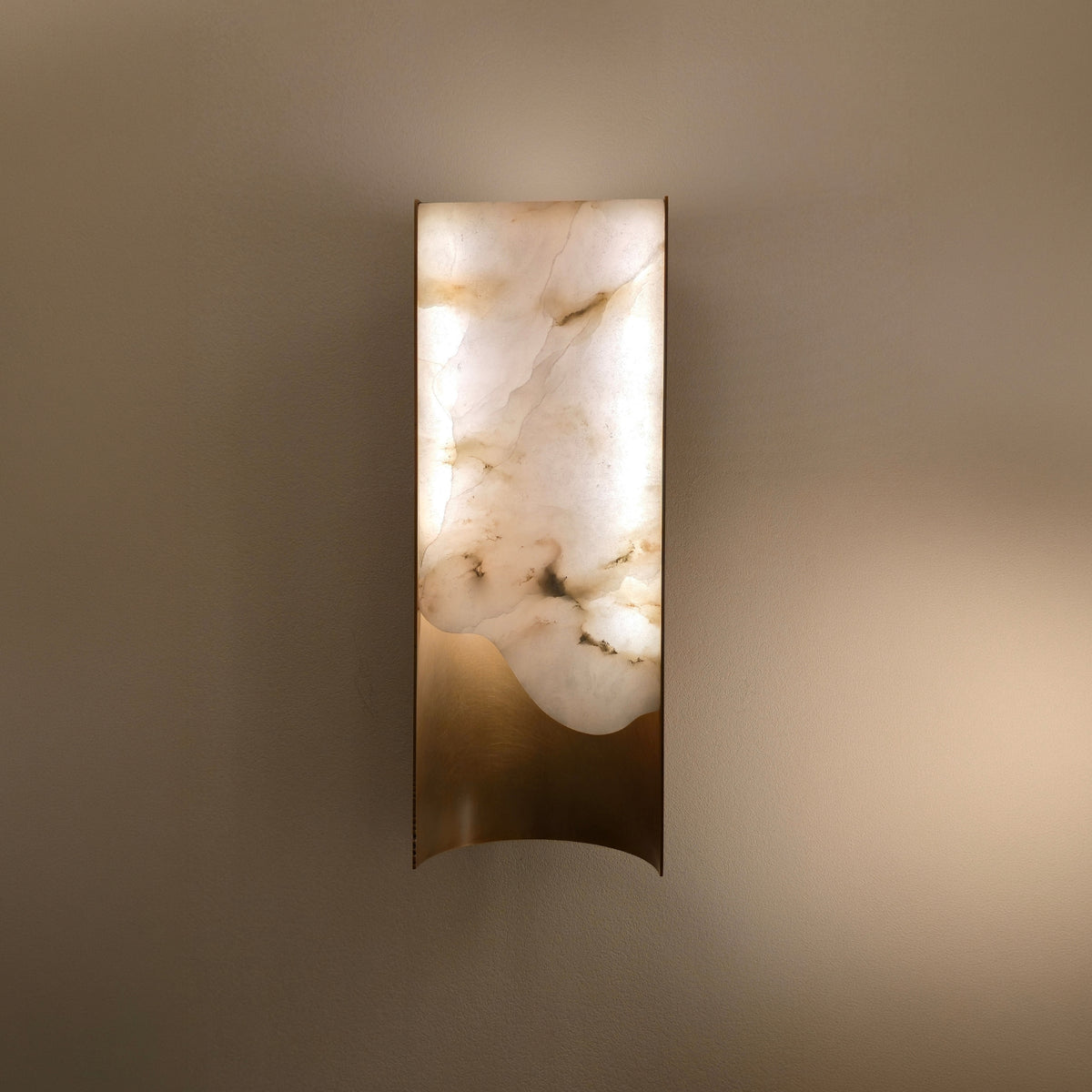Caelith 1 Light Small Carved Alabaster Wall Light in Brushed Brass, glowing rectangular alabaster panel with visible veining, mounted on a neutral wall.