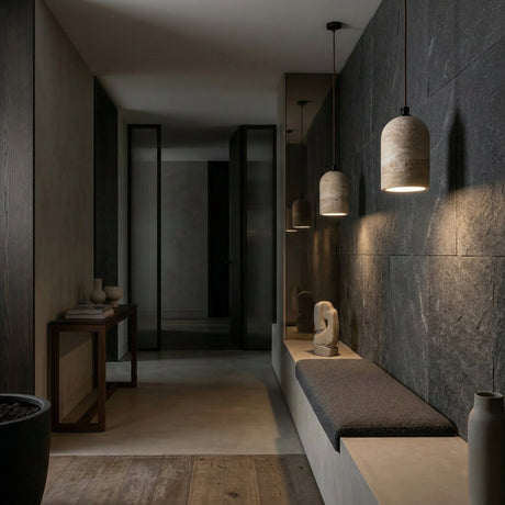 A modern hallway with dark slate walls, a minimalist bench, wood and stone accents, and the Belvora 1 Light Capsule Dome Travertine Pendant Light in light beige, plus vases and sculpture on a narrow table for a calm, sophisticated feel.