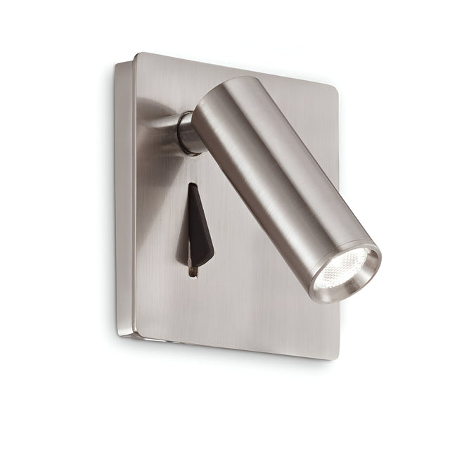 The Ambience LED Wall Spotlight - Nickel features a brushed metal design with a cylindrical shape and polished nickel finish, extending from a rectangular base. It offers adjustable lighting angled downward and includes a small on/off switch on the base.