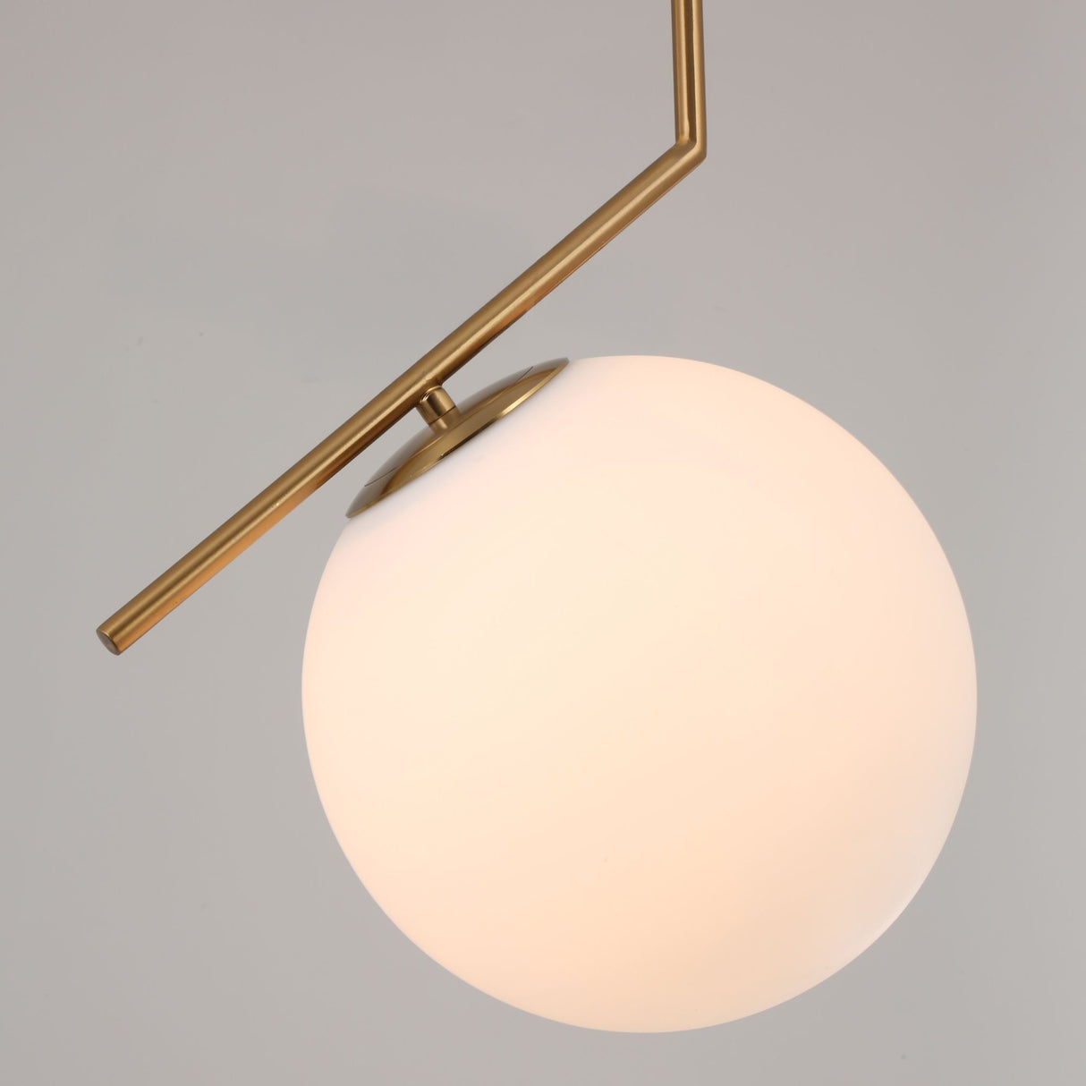 Niori Vetra small pendant light with a white opal glass globe held off-axis by a brushed gold bent metal stem, shown against a plain grey background.
