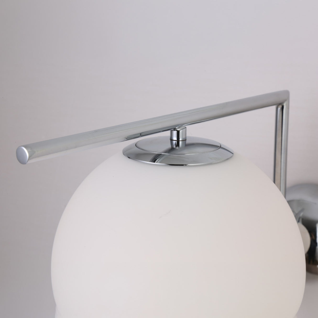 The Vetra 1 Light Opal Glass Wall/Semi-Flush Ceiling Light in grey features a frosted white globe shade and a sleek horizontal chrome rod, evoking modern style against a plain light background.