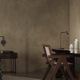 MiniSpot LED Table Lamp in black iron with round base and angled arm, shown on a desk beside a dark wood chair and table in a modern room.