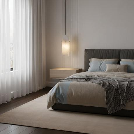 A modern bedroom with a large bed, neutral bedding, a draped blanket, floating nightstand, and wall-mounted lamp. The Lioren 1 Light Vertical Slab Alabaster Pendant hangs above, with sheer white curtains and a beige rug on dark wooden floors.